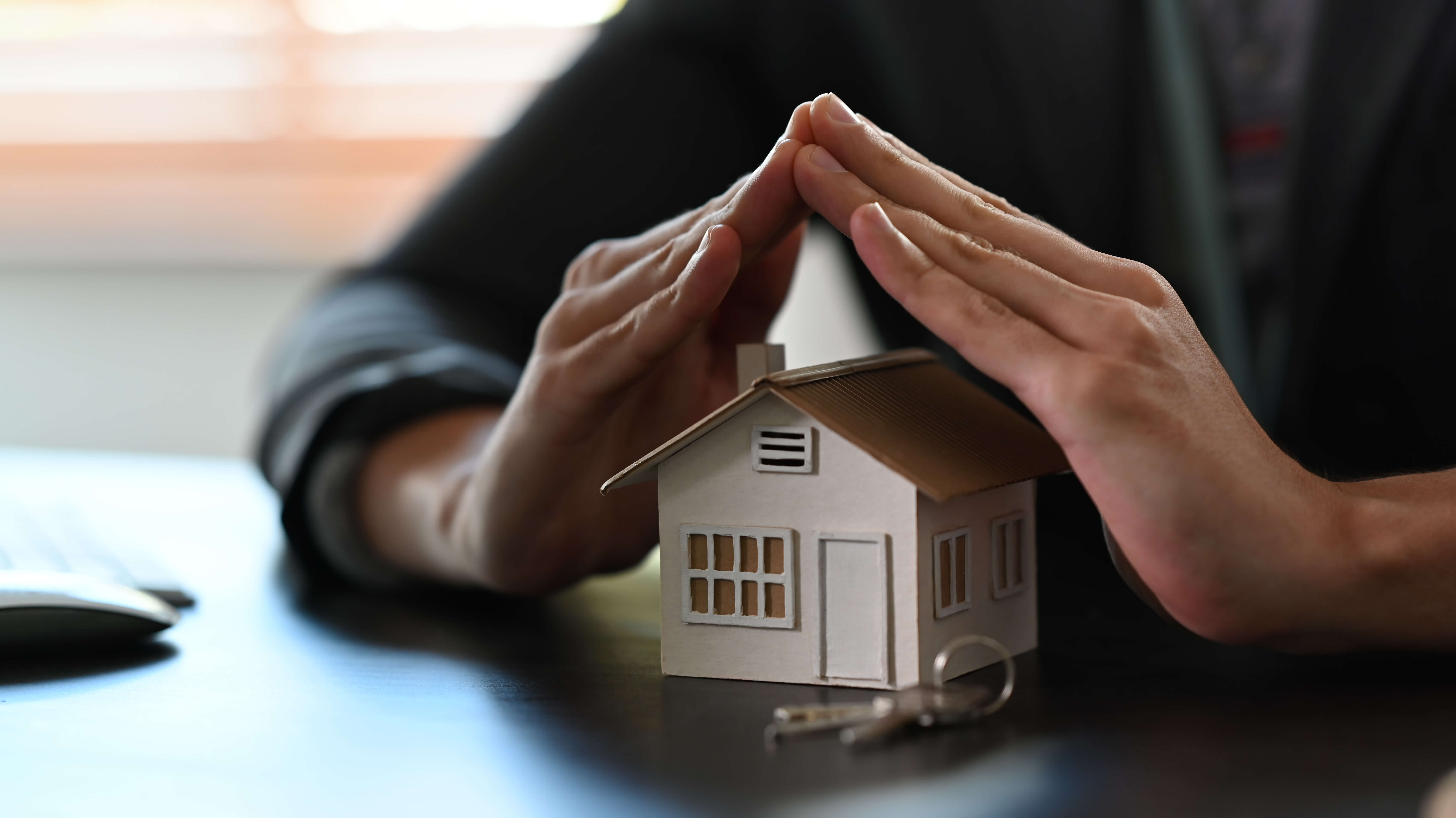 cropped image of small house covered by hands. property insuranc